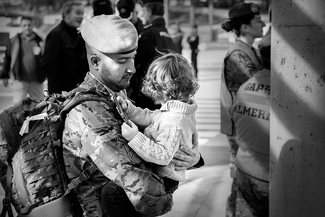 A service member holding a young girl among a crowd.